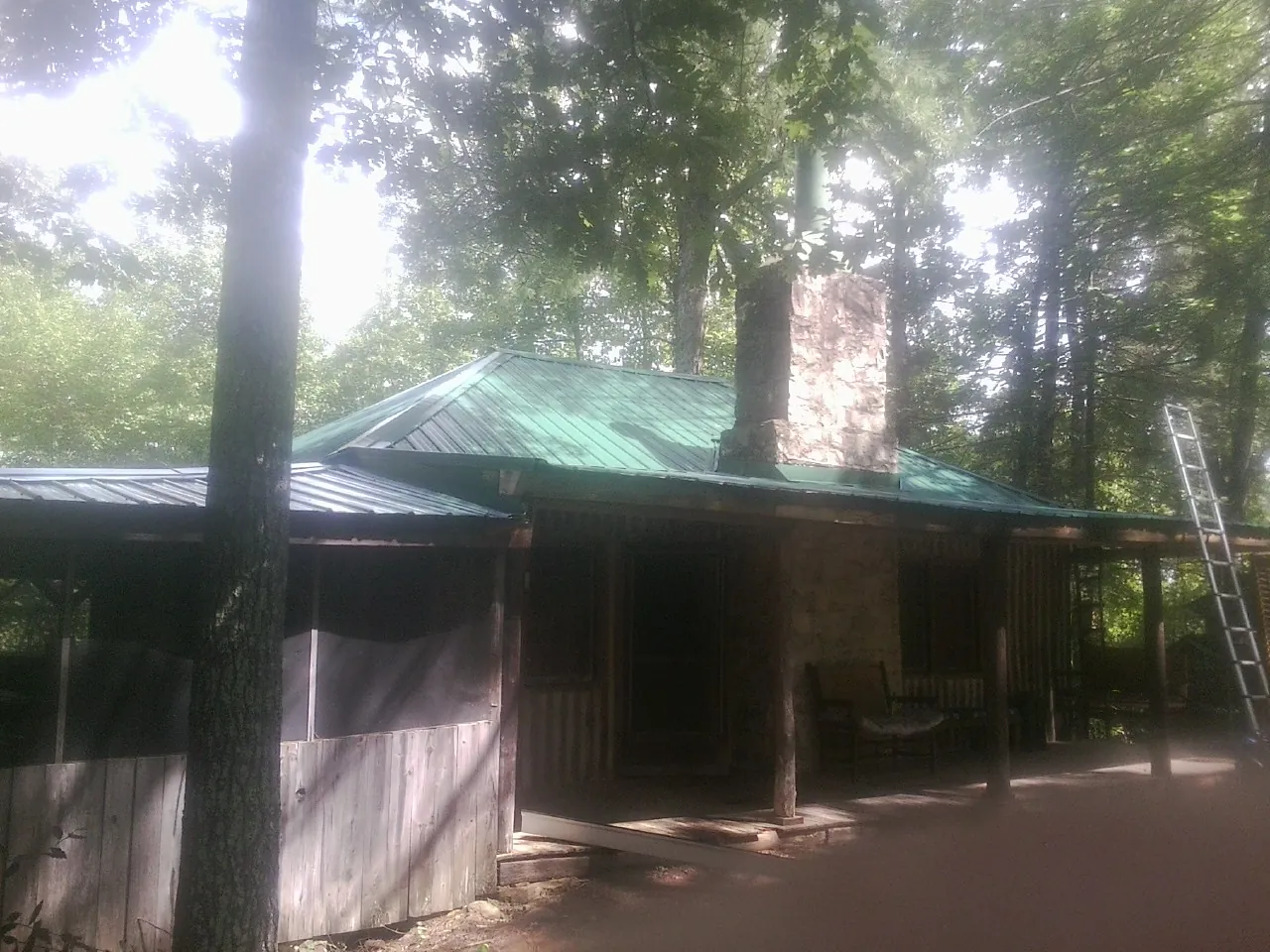 Green metal roof and stone chimney above a log cabin porch in Franklin
