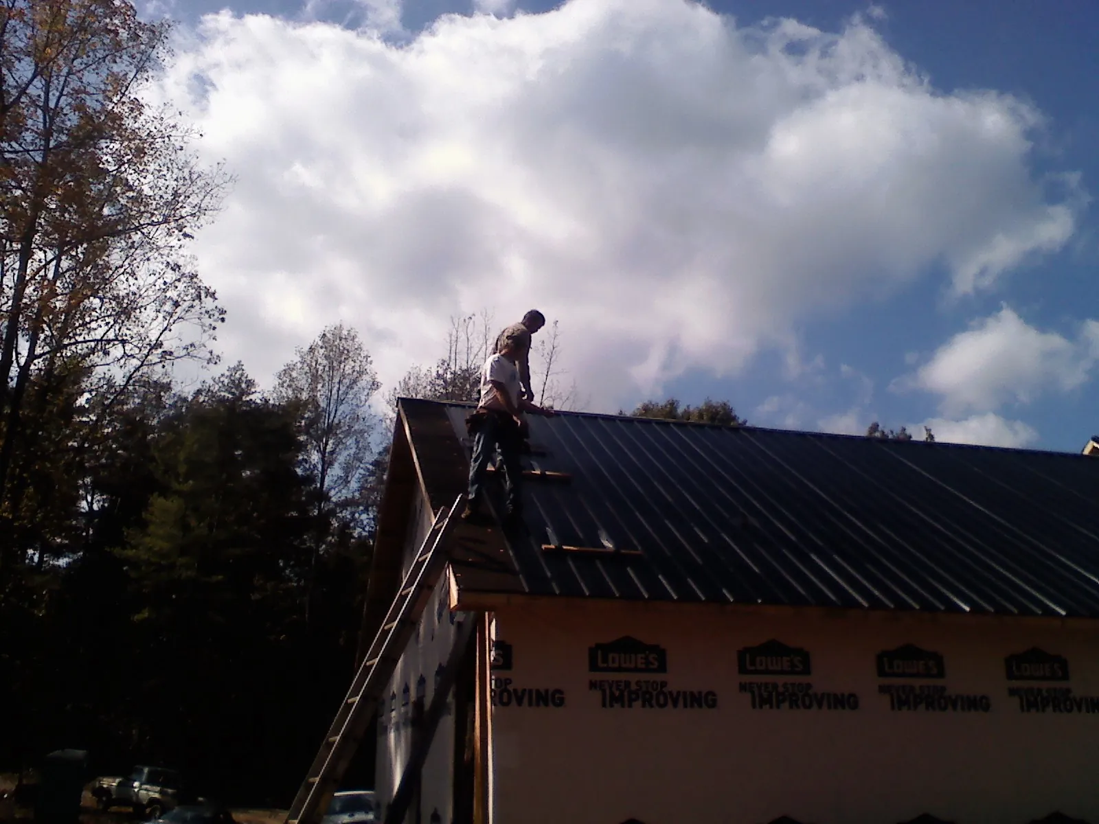 Roofer fastening dark metal panels high against a cloudy sky, from a Roof Inspection job in Franklin
